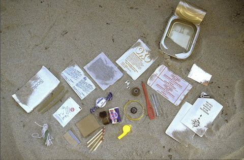 Unpacked Grab-And-Go Survival Kit In A Can 38 Essential Camping And Hiking Tools For Emergencies displayed on sand