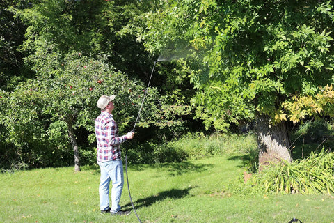 Person using Farm Grade Adjustable Spray Gun With 50 Inch Reach, 18 Orifice, 150 Psi Max, spraying tree branches in garden