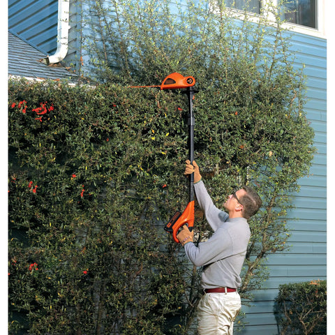 Man using 20V Max Cordless Pole Hedge Trimmer With 18-Inch Dual-Action Blade to trim tall hedges beside a house