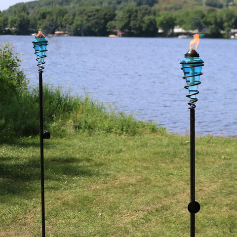 Two Pack Glass Patio Torch Set by the lake with blue glass vessels and metal casings, providing ambient lighting, adjustable height.