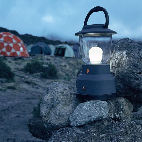 Ultra Bright LED Camping Lantern With 800 Lumens, Battery Powered Emergency Light on rocks with tents in background, evening