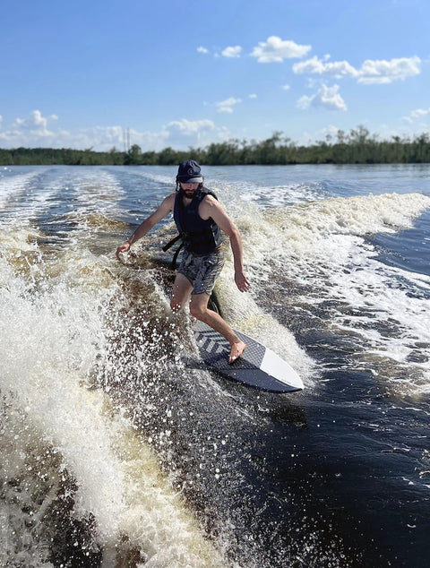 Person surfing on Mondo 5 Foot 2 Inch Wakesurf Board with EVA Padding Thruster Fin Design on a lake wave