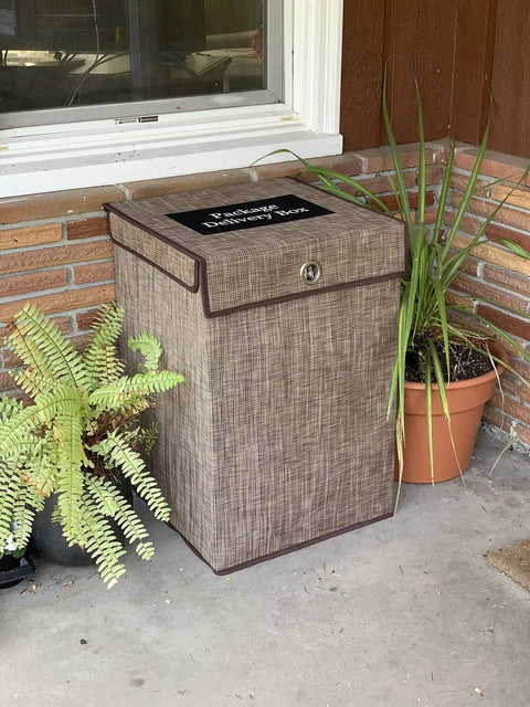 Outdoor Parcel Box Weatherproof Porch Storage Keeps Packages Safe From Rain And Porch Pirates Durable Plastic And Outdoor Fabric Clear Lid Label Reads Deliveries To Help Carriers Spacious 18 By 18 By 26 Inches Interior Brown next to plants on porch