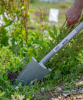 32 Inch Serrated Garden Shovel And Saw Combo removing weeds in a garden, showing curved serrated tip and durable design.
