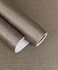 Taupe Metallic Grasscloth Peel And Stick Wallpaper Roll Featuring Faux Woven Texture With Subtle Shimmer on a flat surface.