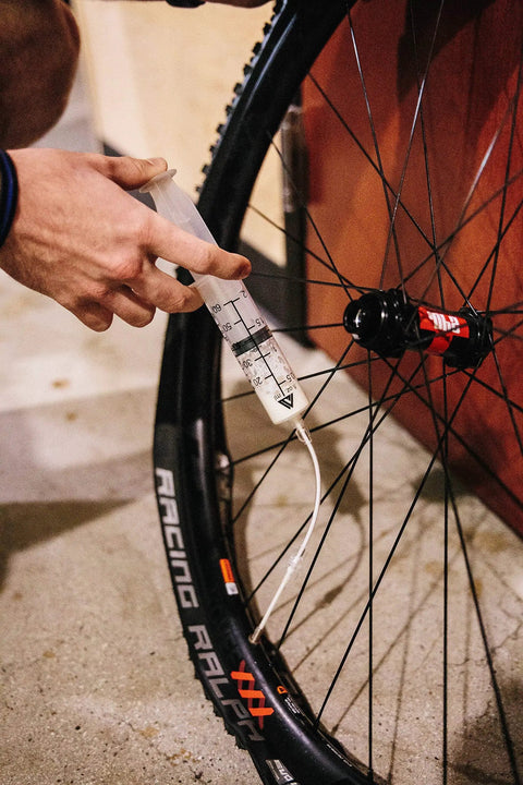 Person using Tubeless Sealant Injector Syringe And Presta Valve Core Removal Tool For Stans No Tubes on a bike tire