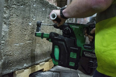 Person using Dust Extraction Attachment For Cordless Rotary Hammer With HEPA Filter on concrete wall, green and black design