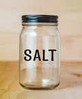 Glass jar labeled 'Salt' with a black lid on a wooden surface