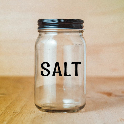Glass jar labeled 'Salt' with a black lid on a wooden surface