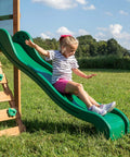 Child sliding on Buckley Hill Cedar Wood Swing Set With Wave Slide, Elevated Play Deck, Rock Wall Ladder, Belt Swings, Chalkboard.