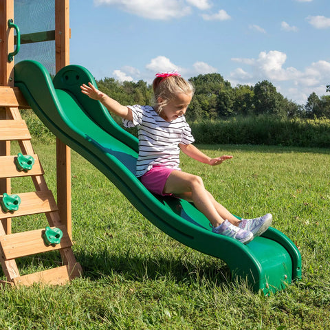 Child sliding on Buckley Hill Cedar Wood Swing Set With Wave Slide, Elevated Play Deck, Rock Wall Ladder, Belt Swings, Chalkboard.
