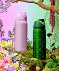 Pink and green FreeSip Insulated Stainless Steel Water Bottles with straws, set in a floral garden background
