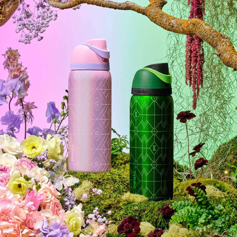 Pink and green FreeSip Insulated Stainless Steel Water Bottles with straws, set in a floral garden background