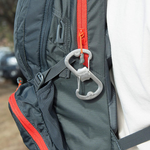 Dual Bottle Opener And SBiner Carabiner Combo In Stainless Steel attached to a backpack near a red zipper.