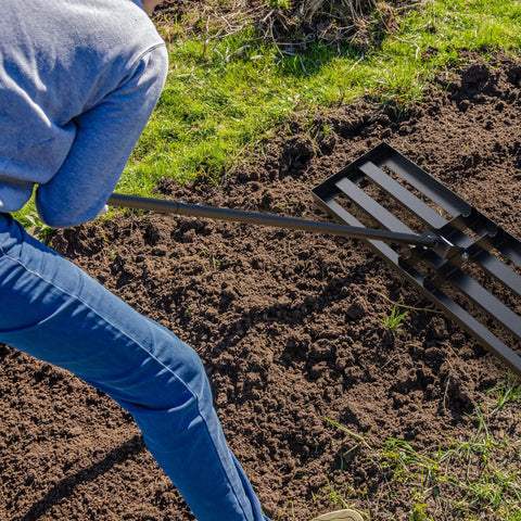 Person using a Heavy Duty Lawn Leveling Rake With 36 Inch Head and 7.2 Ft Handle on soil, showing metal head and long handle.