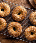 Real Deal Commercial Cooling Rack Set Of 2 With 10 By 18 Inch Cross Wire Baking Grid Built Tough From Durable Chrome Steel and Oven Safe Pedestal Feet That Slide Smoothly Inside Standard Sheet Pan Trays holding six freshly baked bagels.