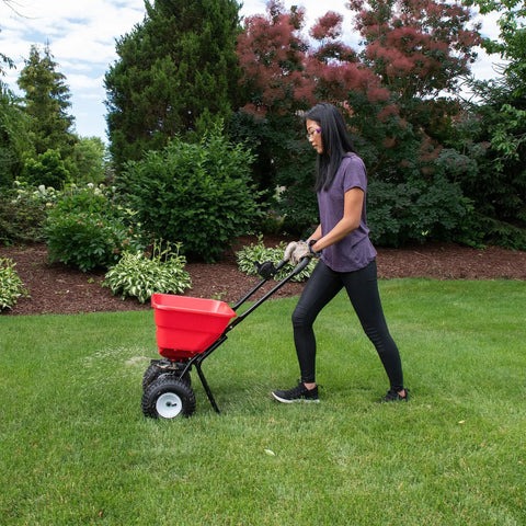 Person using Big 80lb Capacity Broadcast Spreader For Lawns And Seeds With Rustproof Poly Hopper Pre Assembled Adjustable Drop