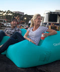 People sitting on Inflatable Lounger Air Chair Lightweight Self Inflating Beach Chair with pockets, teal color, in outdoor setting.
