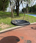 Black heavy duty swing seat with weatherproof ropes, in a backyard setting, showcasing adjustable height feature for adults and kids.