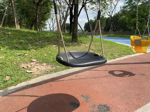 Black heavy duty swing seat with weatherproof ropes, in a backyard setting, showcasing adjustable height feature for adults and kids.
