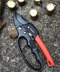 Badass Heavy Duty Anvil Pruning Shears 8 Inch Blade Ratchet Action Pruner on stone surface with cut branches nearby.