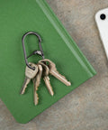 G Series Dual Chamber Carabiner Size 2 1 Pack Black holding keys on green notebook next to smartphone