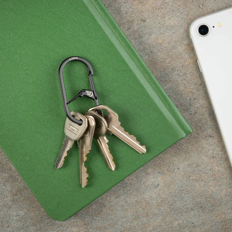 G Series Dual Chamber Carabiner Size 2 1 Pack Black holding keys on green notebook next to smartphone