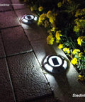Solar Deck Lights 12 Pack White Solar Powered Outdoor LED Path Markers illuminating a pathway at night, surrounded by flowers.