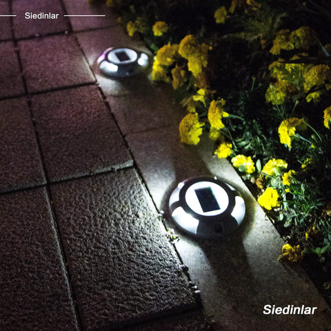 Solar Deck Lights 12 Pack White Solar Powered Outdoor LED Path Markers illuminating a pathway at night, surrounded by flowers.