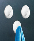 Heavy Duty Adhesive Wall Hooks For Bathroom And Kitchen Built Tough With Super Grip Oil Resistant Plastic Surface Mounts Zero Hole Punch Needed Fully Waterproof Set Of Three White Units with a blue towel hanging on a smooth surface.