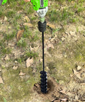 Garden auger drill bit attached to green cordless drill, drilling into soil for planting