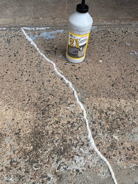 Bottle of 2X Concrete Crack Sealant Easy To Use No Mess Ready Mixed Filler For Cracks Up To Half Inch next to a filled crack on concrete