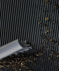 Cleaning Heavy Duty Vinyl Round Rib Floor Mat For Tough Garages And Workshops with brush, showcasing dirt and debris.