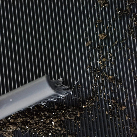 Cleaning Heavy Duty Vinyl Round Rib Floor Mat For Tough Garages And Workshops with brush, showcasing dirt and debris.