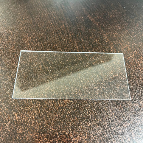 Clear plastic lens cover for welding helmet, size 2x4.25 inches, on dark table. 25 Pack Clear Lens Covers For Welding Helmet Hood 2 In By 4.25 In Replacement Auto Darkening Lens Shield Keeps Your Shield Scratch Free And In Top Shape For Everyday Maintenance.