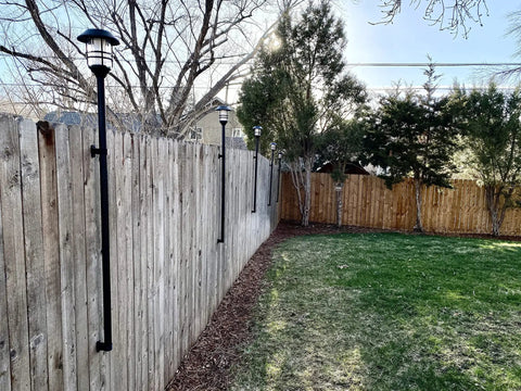 Deck Or Fence Mount For Tiki Torches And 1-1/4-Inch Poles Fits Solar Lights Black Outdoor Torch Bracket With Ground Clearance And Vertical Mount Keeps Deck Surfaces Clutter-Free installed on wooden fence.