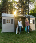 Two people exiting Desert Sand Outdoor Storage Shed 15x8 Ft Resin Backyard Tool Shed with lockable doors and UV-protected panels