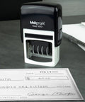Built Tough Self Inking Date Stamp With Bright Red Ink And Big Bold Four Millimeter Dates on a desk next to a check.