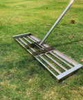 Stainless Steel Lawn Leveling Rake With 72 Inch Two Section Handle heavy duty on grass, U shape handle, rubber grip visible.