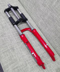 26 Inch Suspension Front Fork With One And One Eighth Inch Headset Disc Brake Ready Aluminum Triple Tree Red Travel 90 100mm 28.6mm Threadless Steerer 50mm Disc Mount Fits Mountain Bikes displayed on gray sofa