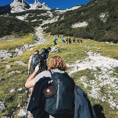 Group hiking on a mountain trail with Mini First Aid Kit 120 Piece Waterproof Hard Shell Medical Kit attached to a backpack.