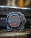 1-3/16 Inch By 25 Foot Dual Sided Tape Measure With Nite Eye Glow resting vertically on a wooden surface