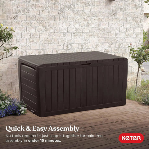 71 Gallon Outdoor Resin Storage Box For Patio Cushions And Throw Pillows, shown as a brown chest on a wooden deck with plants.