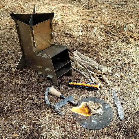 Outdoor scene with FireRope Tinder Weatherproof Firestarter, small stove, and camping tools on forest floor for quick ignition.