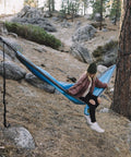 Person sitting on hammock with heavy duty hammock straps for trees 10 foot kit with carabiners and 38 loops setup between trees.