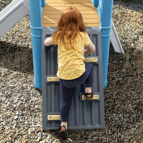 Child climbing on vintage style outdoor kids playset with climber and slide for backyard adventures featuring a climbing wall.