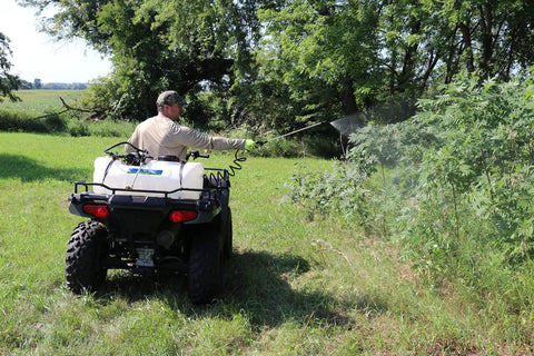 15 Gallon ATV Boomless Broadcast Sprayer With 16 Foot Swath mounted on ATV in field, user spraying foliage