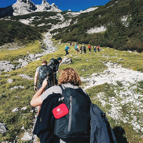 Red 120-piece mini first aid kit attached to a hiking backpack on a rocky mountain trail