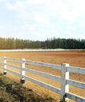 Open field with white wooden fence under clear sky