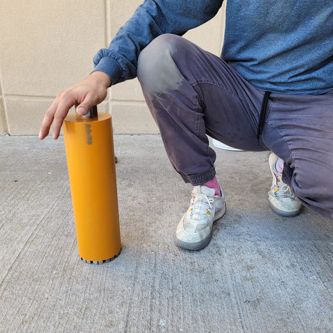 Person holding Turbo Diamond Core Drill Bit 4-1/2 Inch For Concrete And Masonry, 14 Inch Depth, with laser welded teeth on a sidewalk.